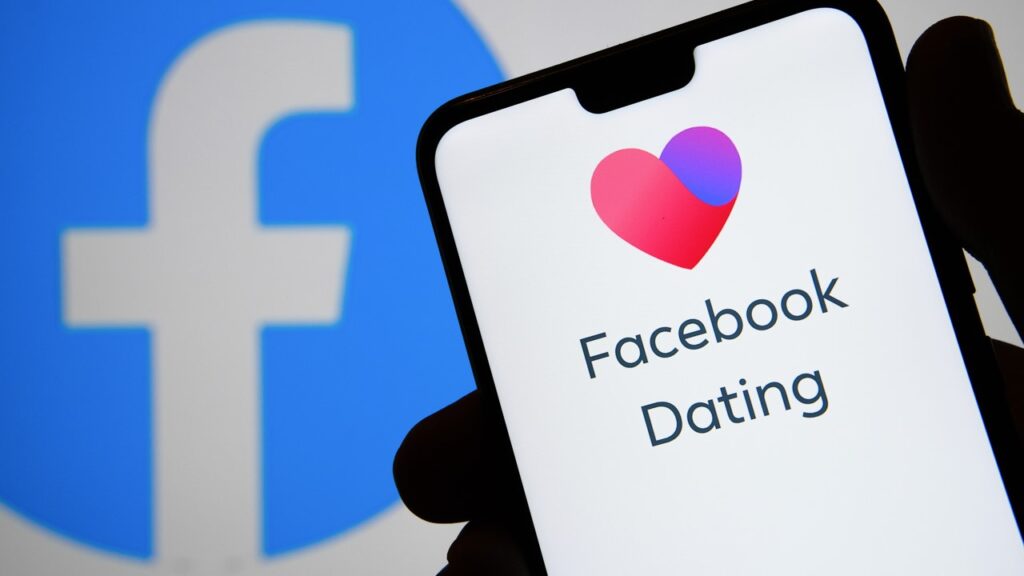 Mão segurando celular com logo do aplicativo Facebook Dating