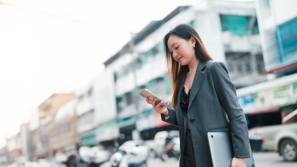 Mulher de negócios sorrindo andando na rua e olhando celular